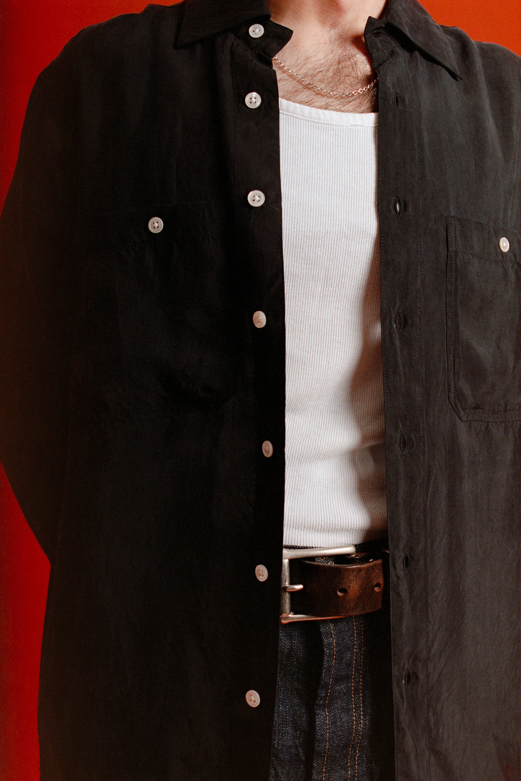 Person wearing a black button-up shirt over a white vest with a red background