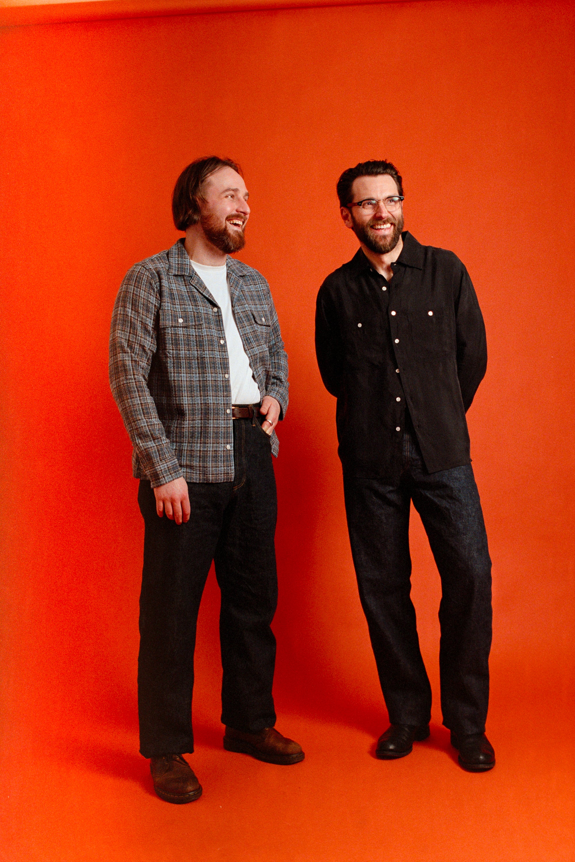 Two men standing against an orange background