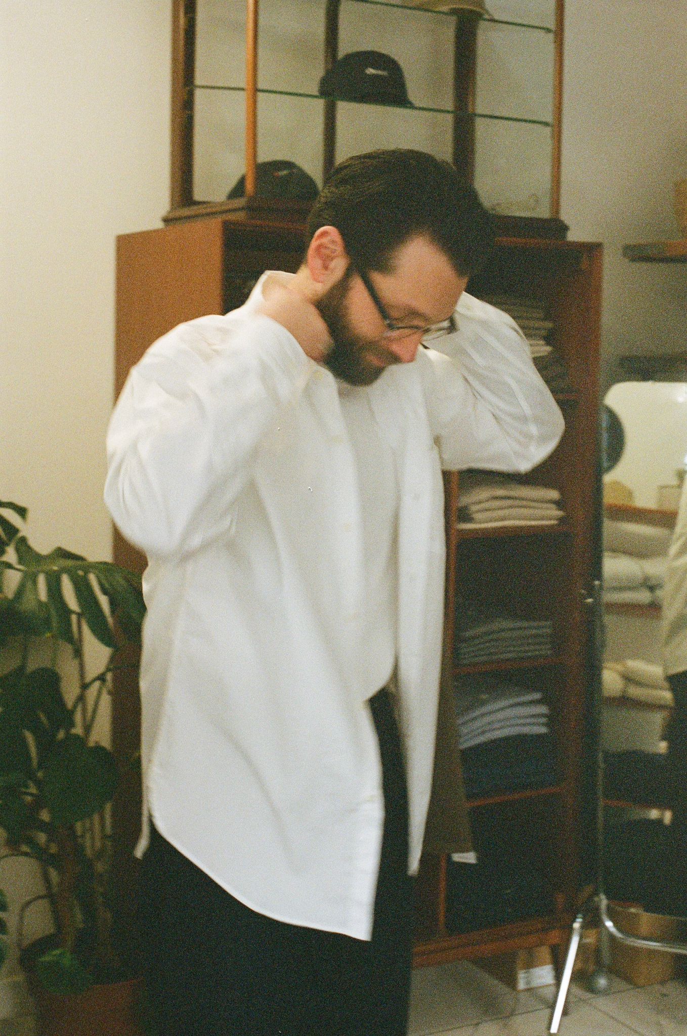 Man adjusting shirt in a room with shelves and plants