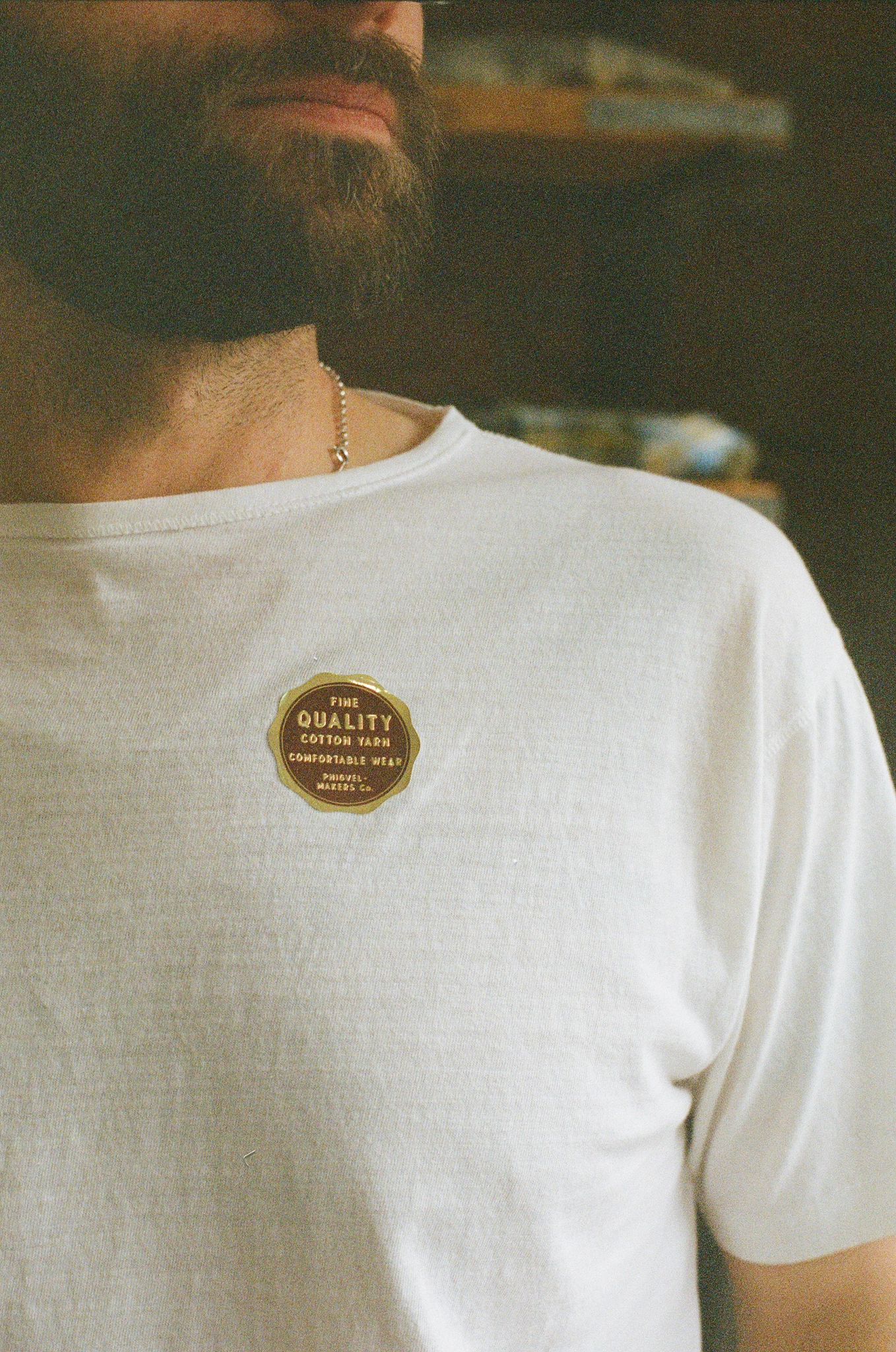 Man wearing phigvel white t-shirt with a gold sticker on the chest.